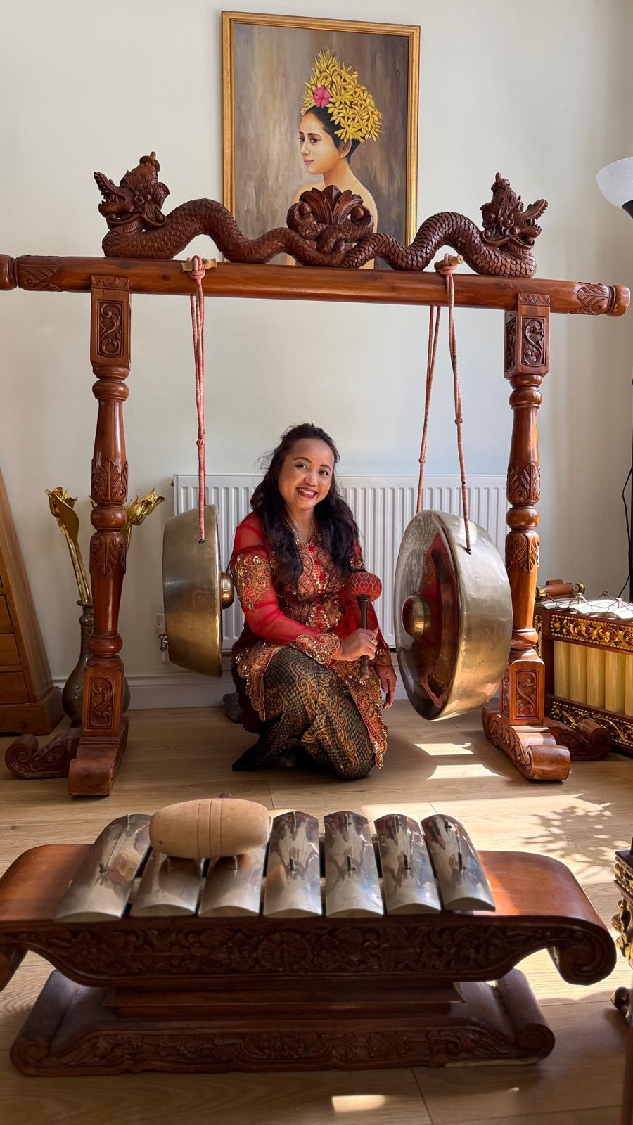 Elis Brown in traditional Indonesian dress beside gamelan instruments